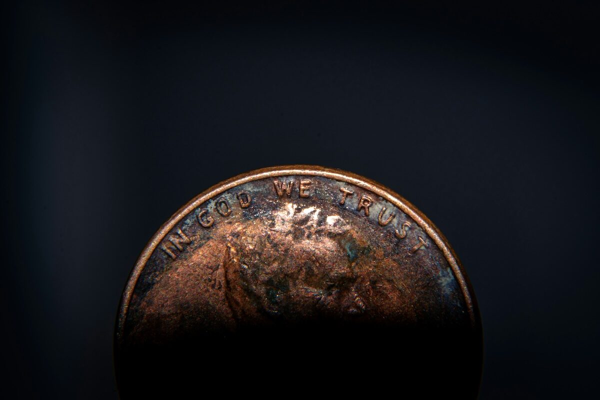 Close-up of the top edge of a worn coin, with the words IN GOD WE TRUST partially visible and the lower part obscured by shadow.