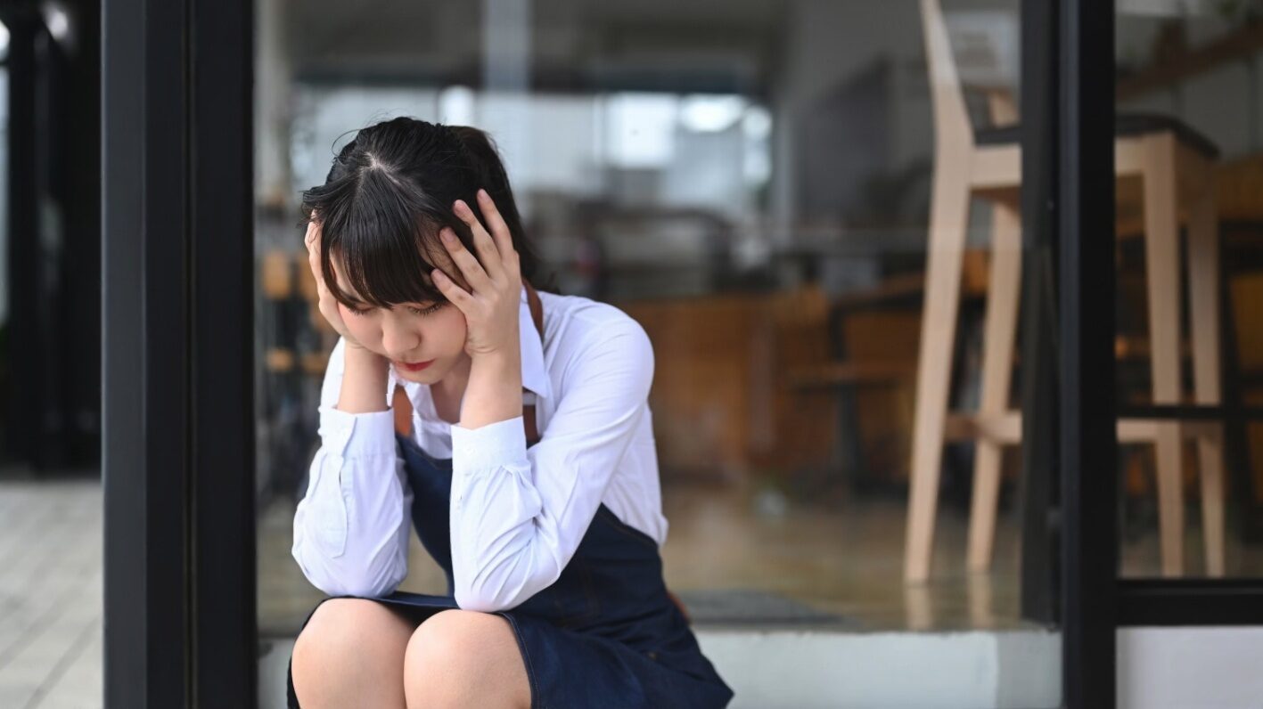 Young woman sitting on steps, looking stressed and sad.