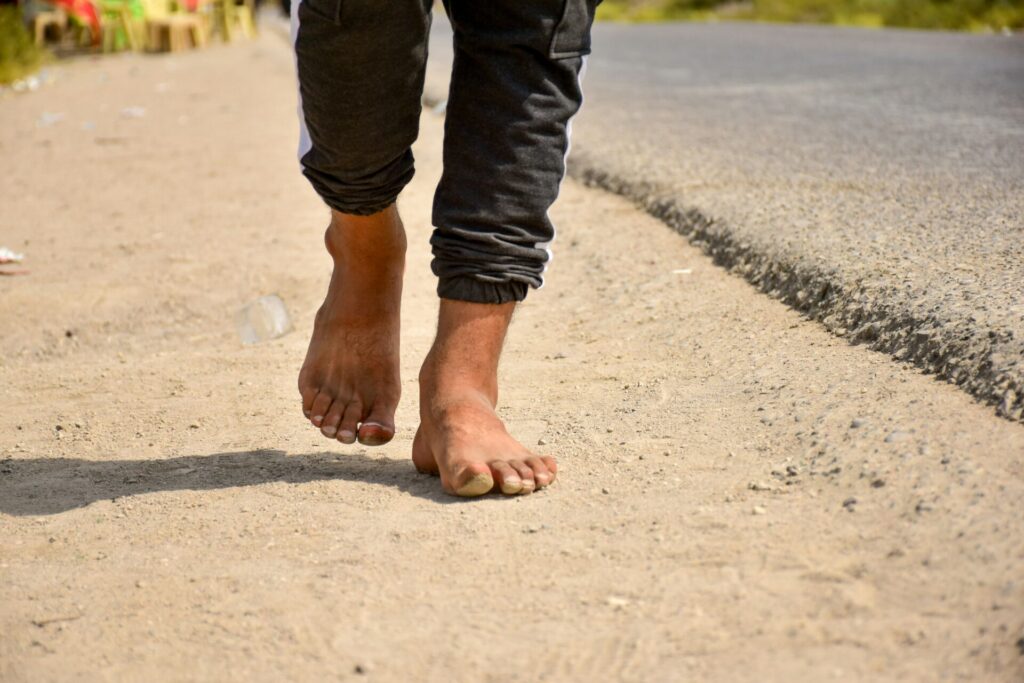 A person in black pants walking in the dirt during daytime