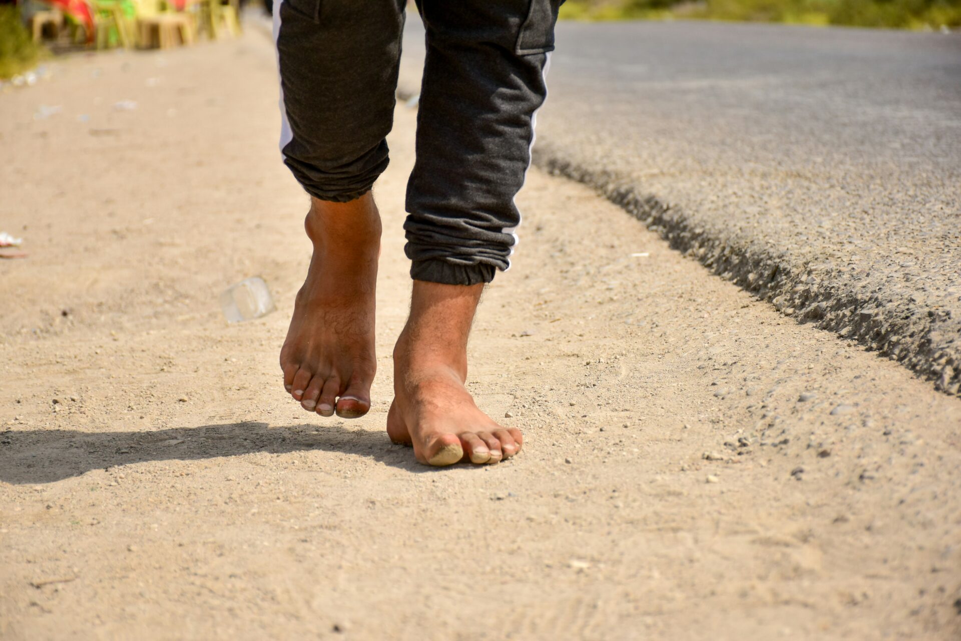 A person in black pants walking in the dirt during daytime