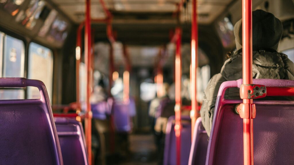 Photo taken looking down the aisle of a bus will orange polls and purple seats