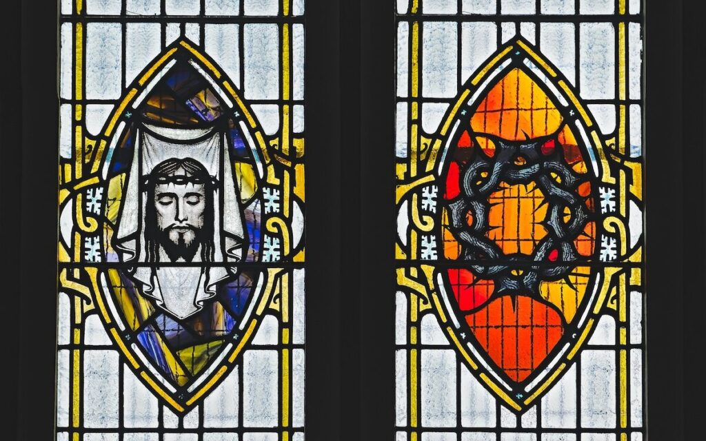 Stained glass window featuring an image of a mans face with a crown of thorns on the left and a crown of thorns on a red background on the right.