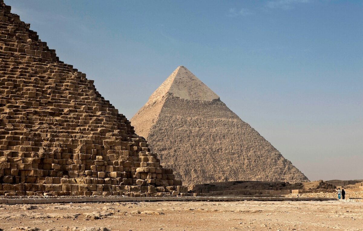 Two large pyramids stand in a desert landscape under a clear sky, with a person visible for scale near the base on the right.