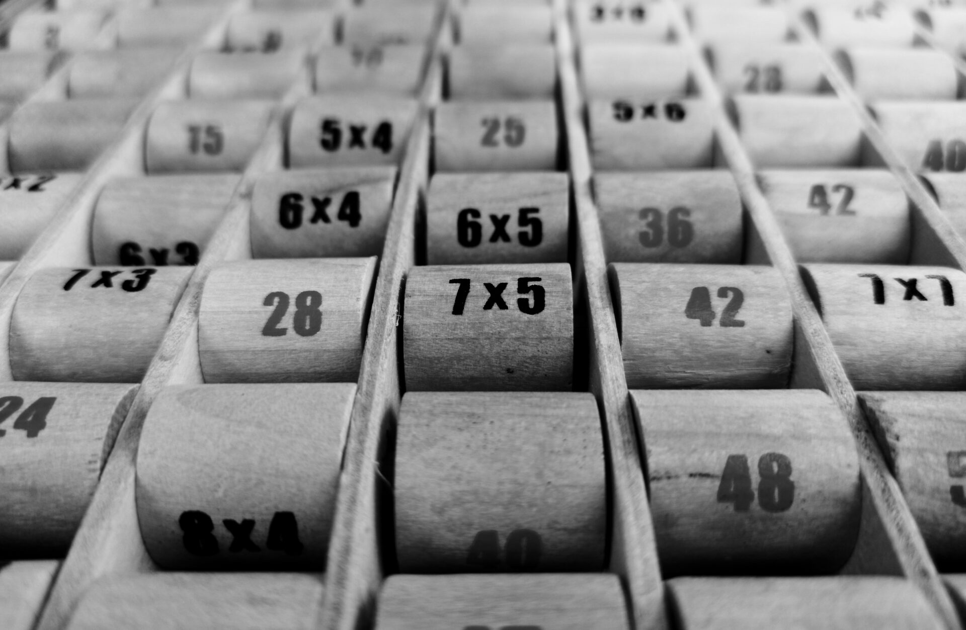Rows of numbered wooden cylinders in compartments, some with multiplication equations and others with numerical answers, arranged in a grid pattern.