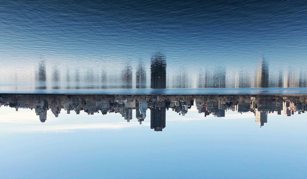 A city skyline is reflected on a large body of water.