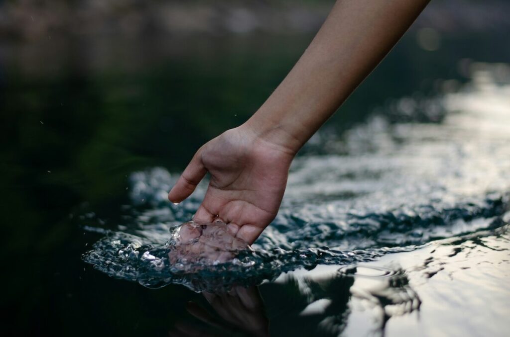 A hand is partially submerged in water, creating ripples on the waters surface.