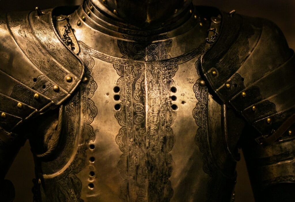Close-up of the chest and shoulders of a detailed, metallic suit of medieval armor with decorative engravings and rivets.