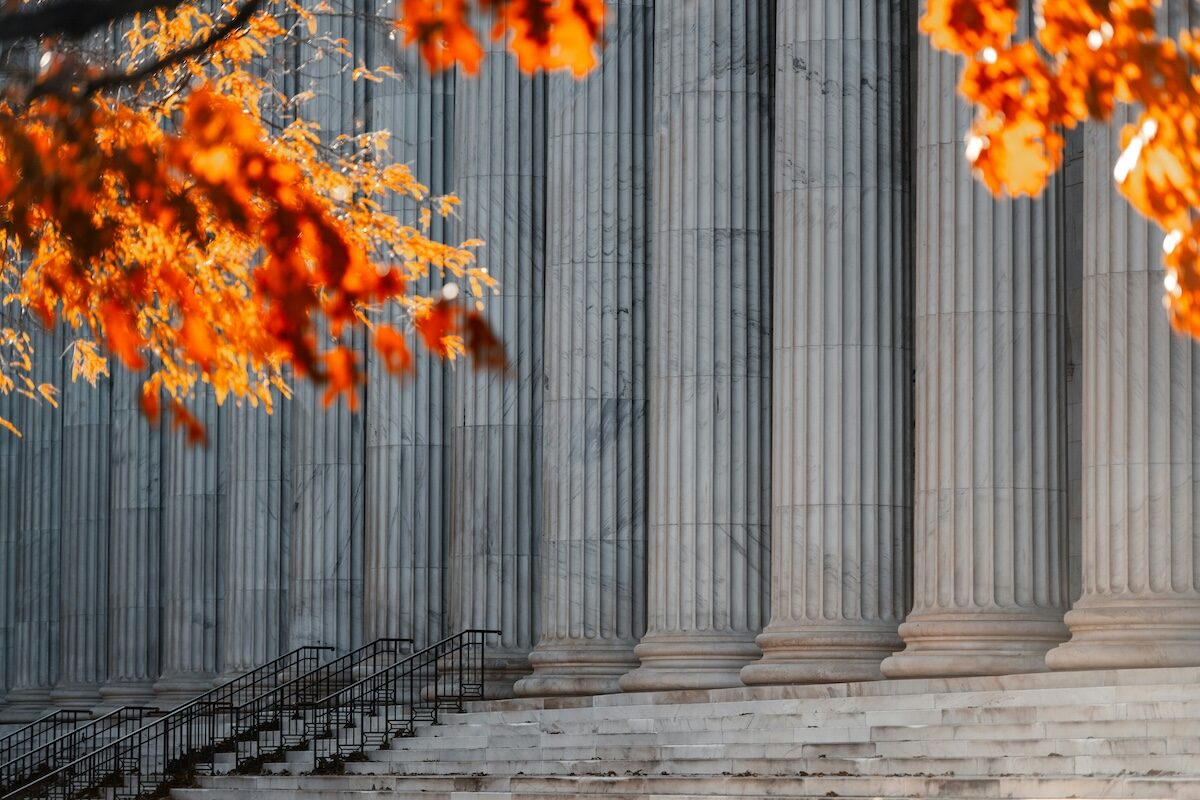 Close-up view of large stone columns with stairs in front, partially framed by autumn leaves in the foreground.