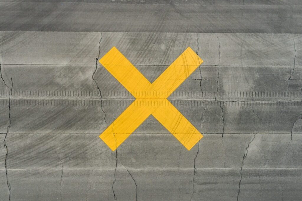 A yellow X is painted on a cracked gray concrete surface with horizontal lines.