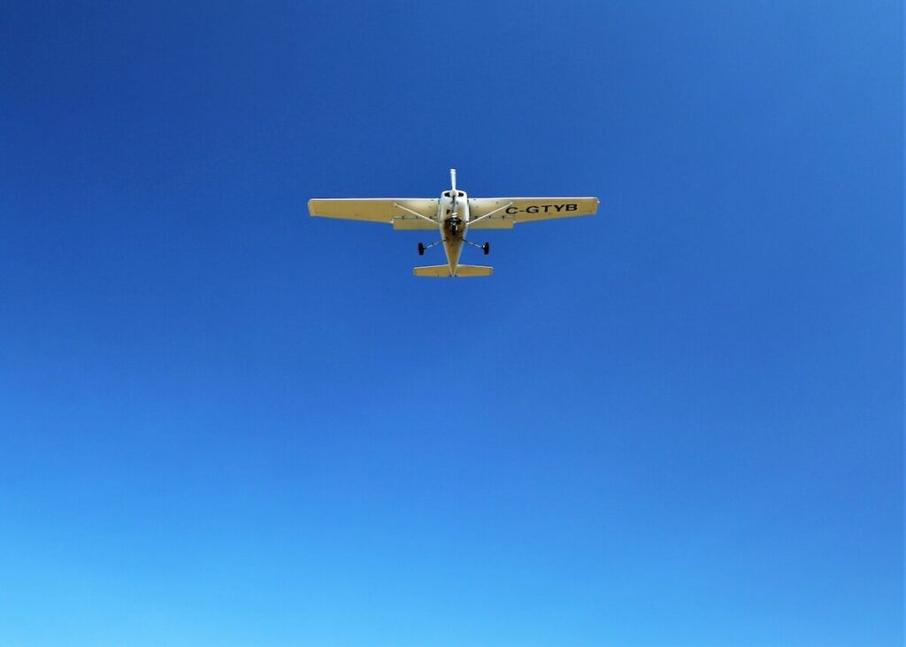 A small single-engine airplane flies across a clear blue sky, viewed from directly below.