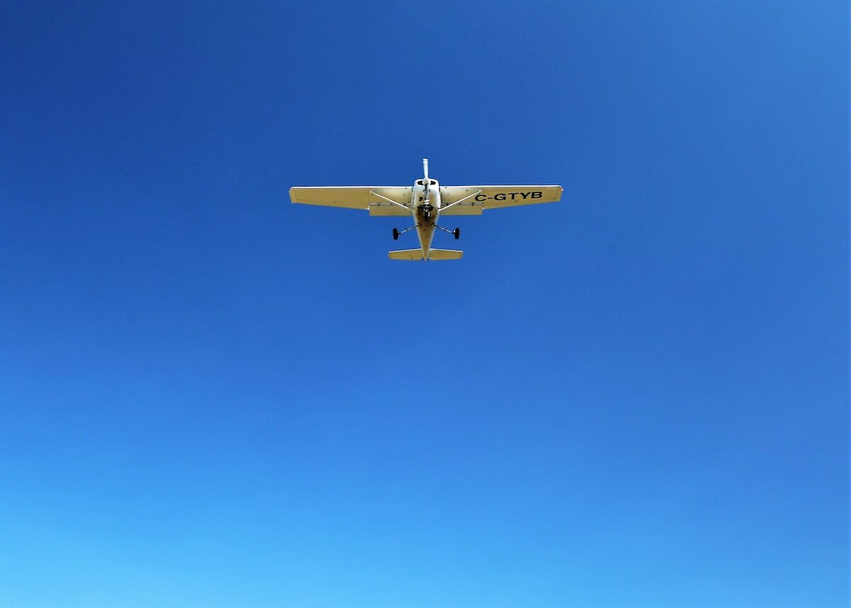 A small single-engine airplane flies across a clear blue sky, viewed from directly below.