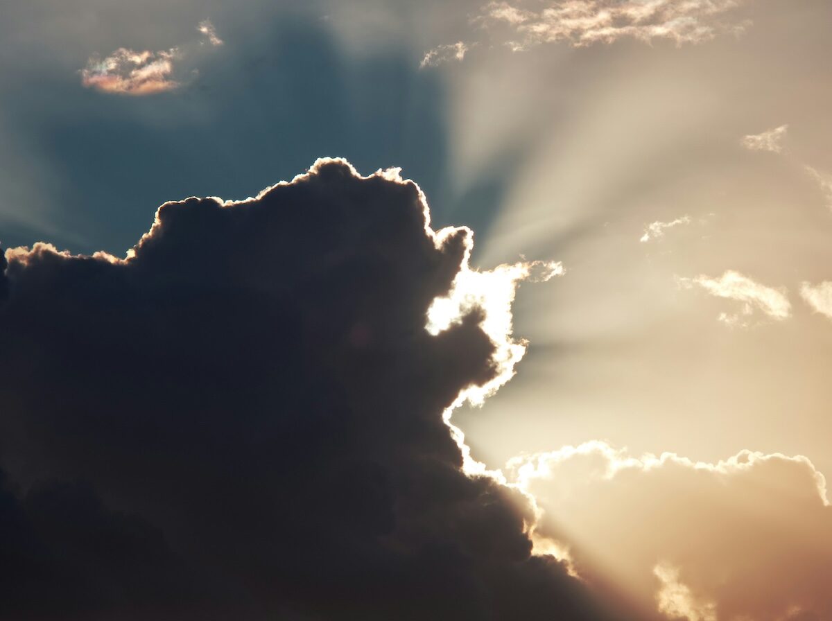 Dark cloud partially obscures the sun, with rays of sunlight streaming out from behind the cloud into the sky.