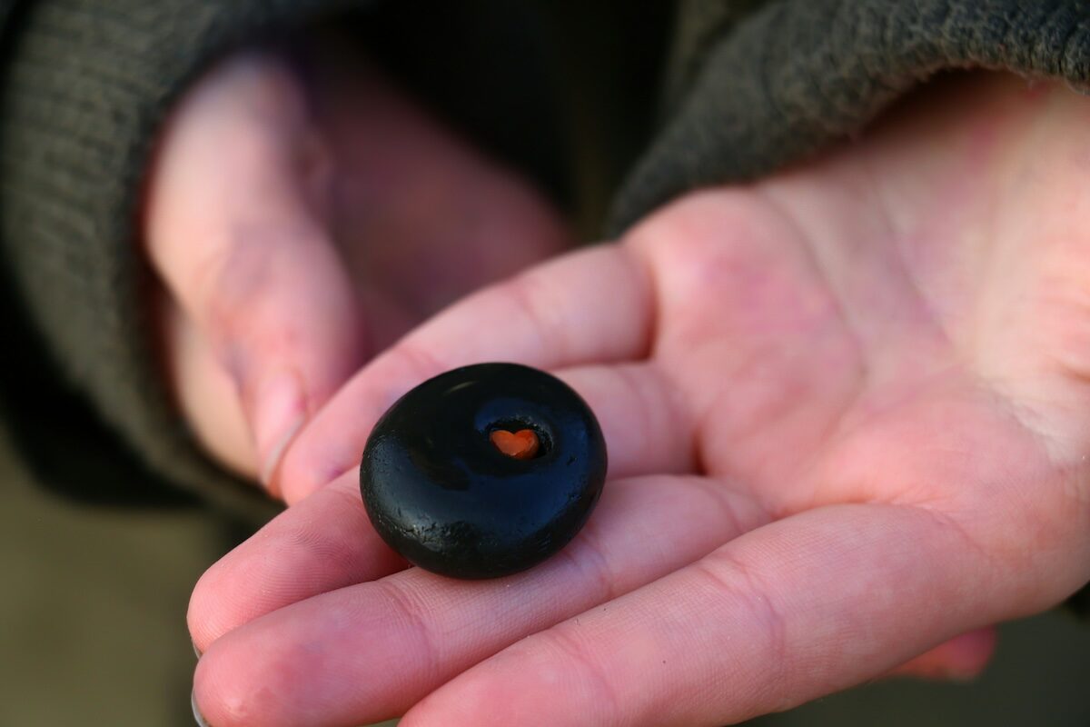 A person holds a smooth, round black stone with a small orange spot in the center in their open palm.