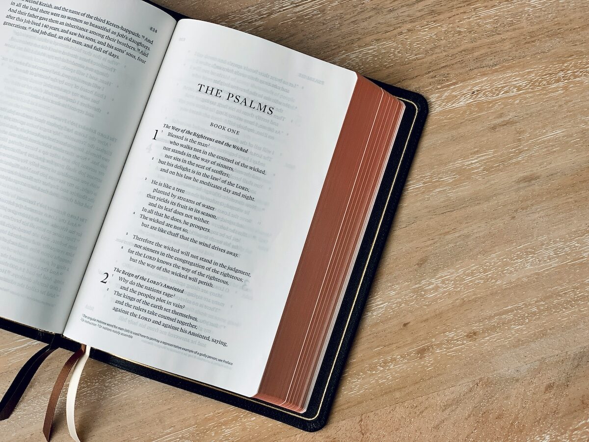 An open Bible lies on a wooden surface, displaying the beginning of the Book of Psalms with ribbon bookmarks visible.