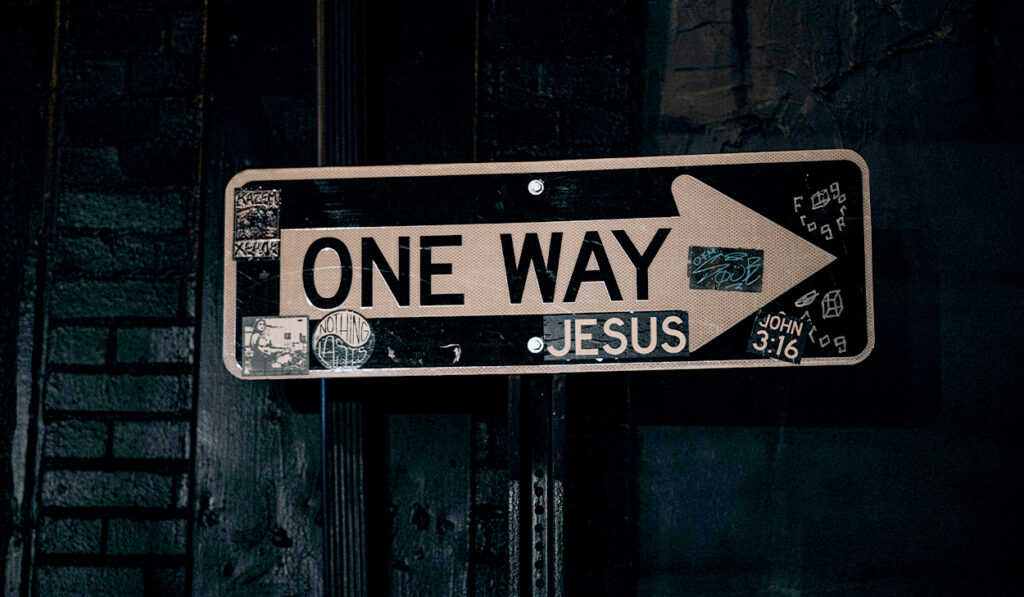 Stickers are posted on a one way sign, including one that says "Jesus."