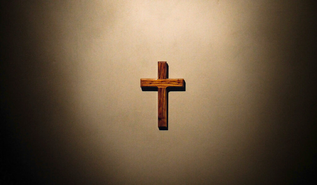 A simple wooden cross hangs on a plain wall.
