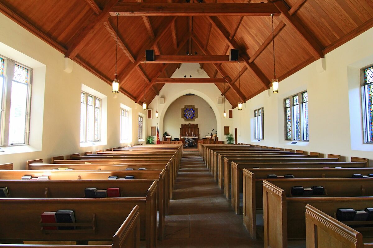 Interior of an empty church with wooden pews, high vaulted ceiling, large windows, and an altar at the front.