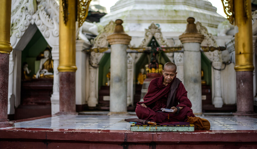 A Buddhist monk sits reading in a temple.