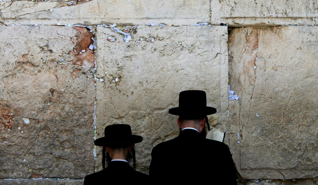 Two Jewish men pray against a wall in Israel.