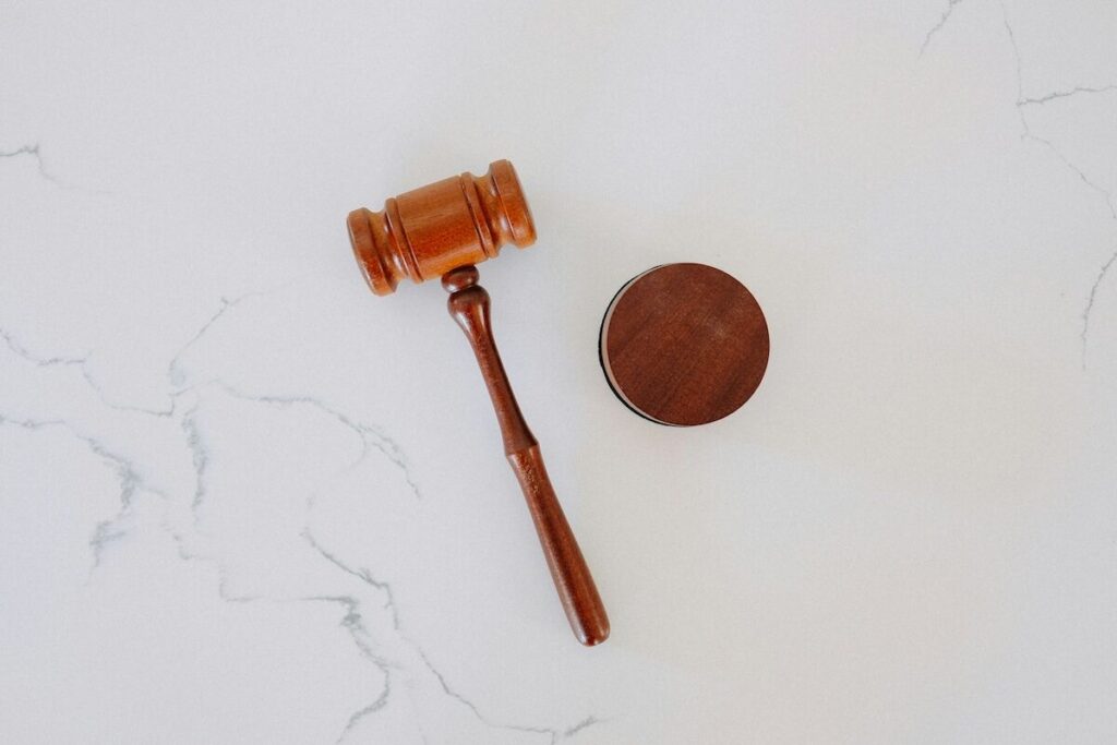 A wooden judge’s gavel and round sound block on a white marble surface.