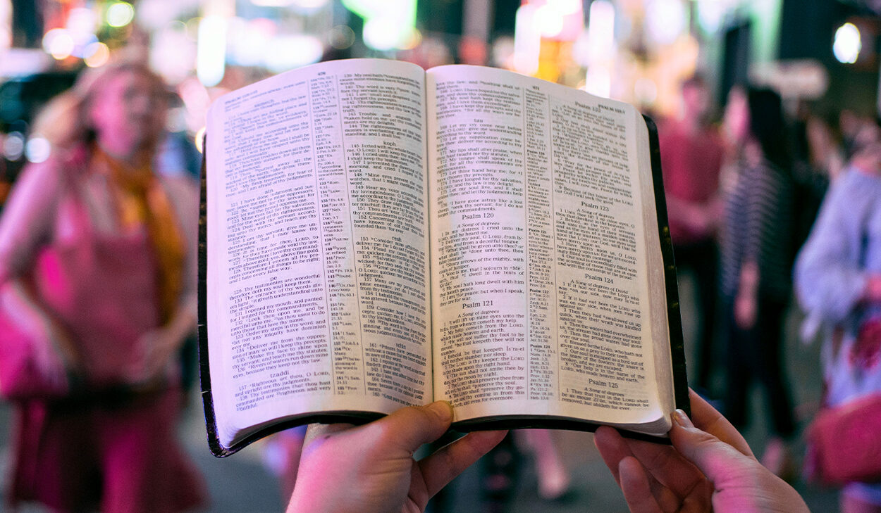 A person stands in a crowded square at night holding up a Bible that is opened to the Psalms.