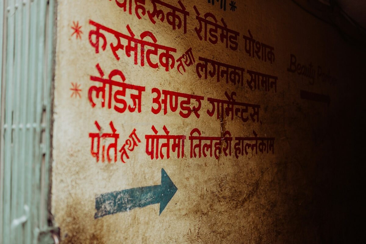 A wall with Nepali text in red and black, including directional instructions, and a blue arrow pointing to the right.