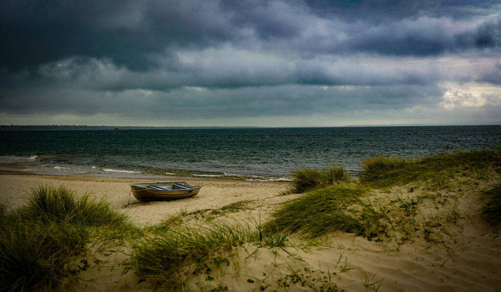 A boat sits on a grassy beach with storm clouds in the background.
