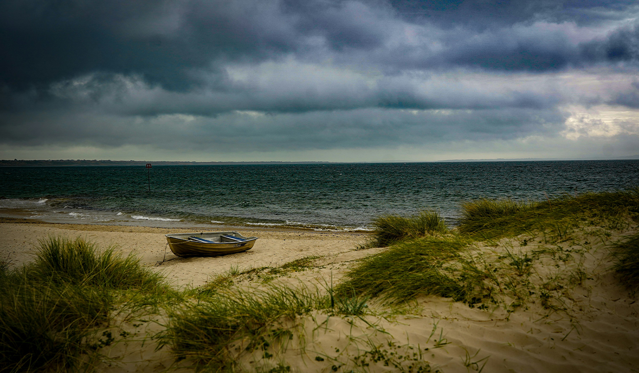 A boat sits on a grassy beach with storm clouds in the background.