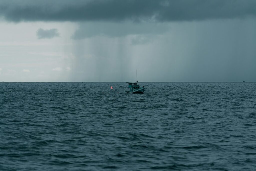 A small fishing boat is floating on a rough sea under a cloudy sky with rain falling in the distance.