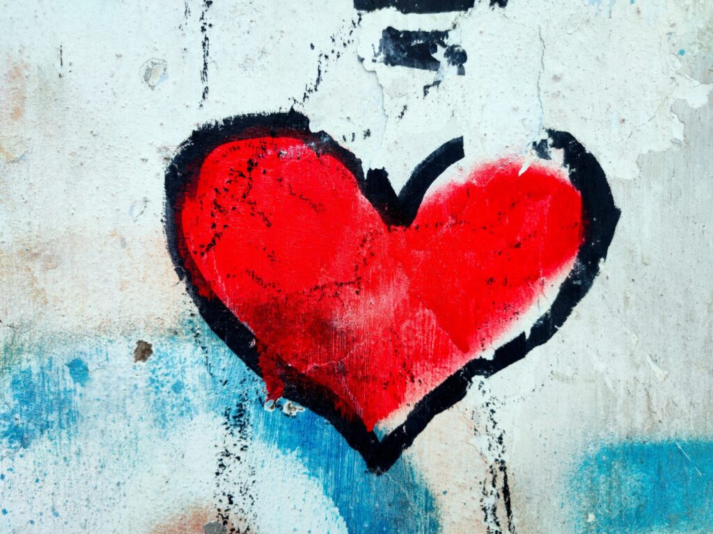 A red heart with a black outline is painted on a weathered, white and blue textured wall.