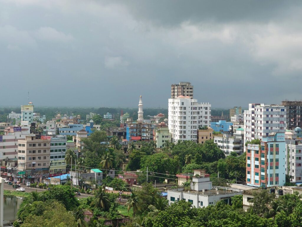 A cityscape with mid-rise buildings surrounded by greenery under a cloudy sky.