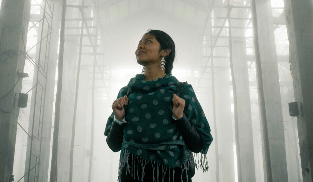 A woman with her dark hair in a braid stands in the middle of a well-lit sanctuary, looking up to the ceiling.