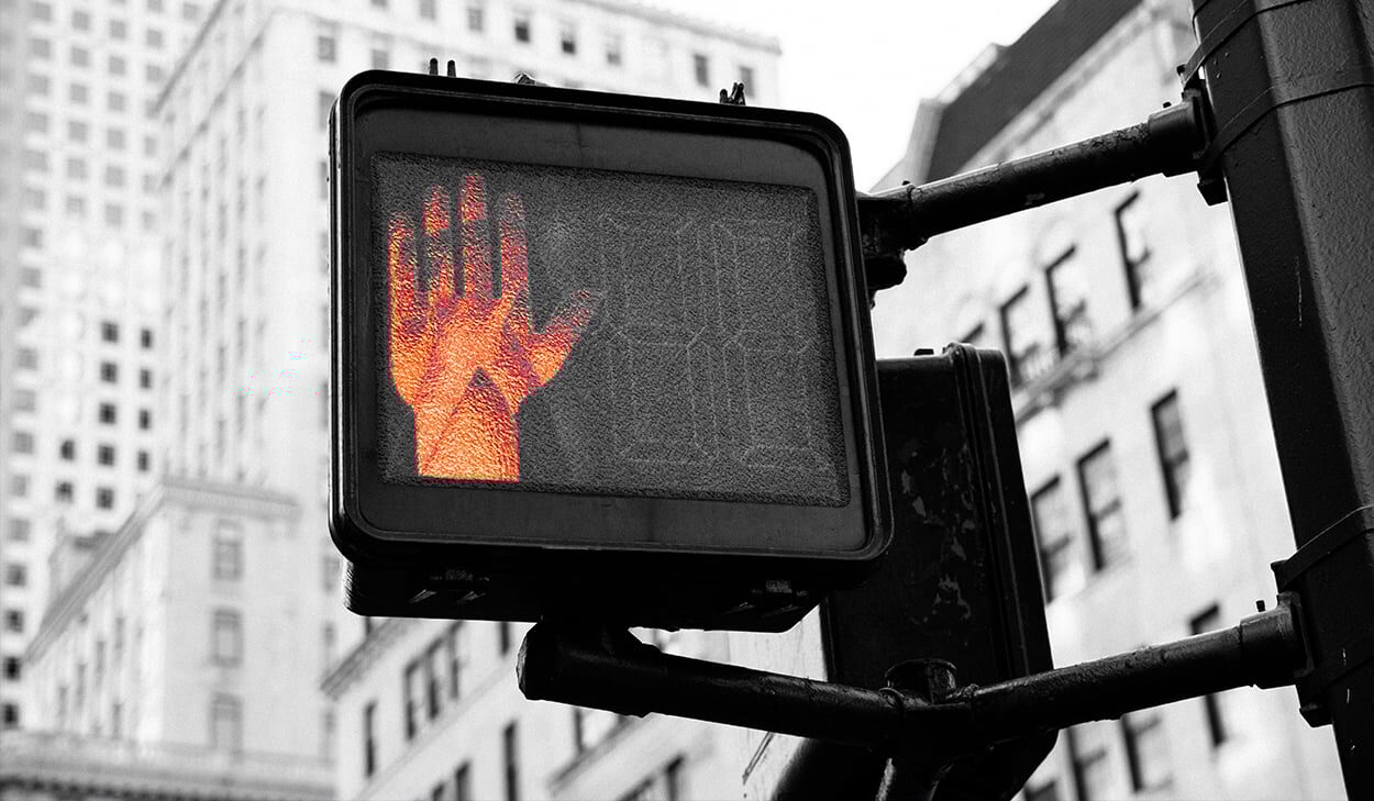 A red hand signal is illuminated on a pedestrian crossing sign in an urban area, indicating that it is not safe to cross the street.