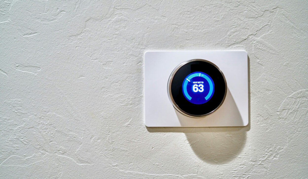 A Nest thermostat sits on a white wall with the temperature set at 63 degrees.