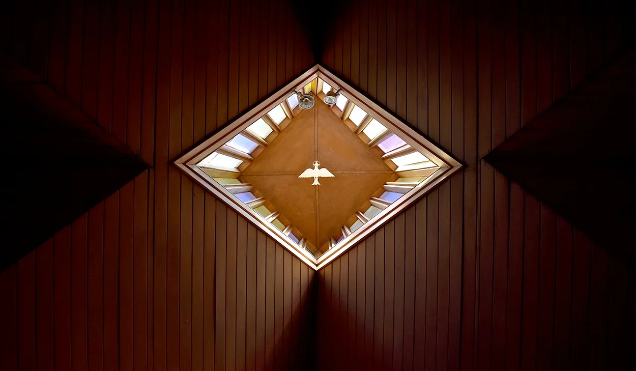 A view looking up at a diamond-shaped skylight with wooden paneling on the ceiling and a hanging light fixture in the center.
