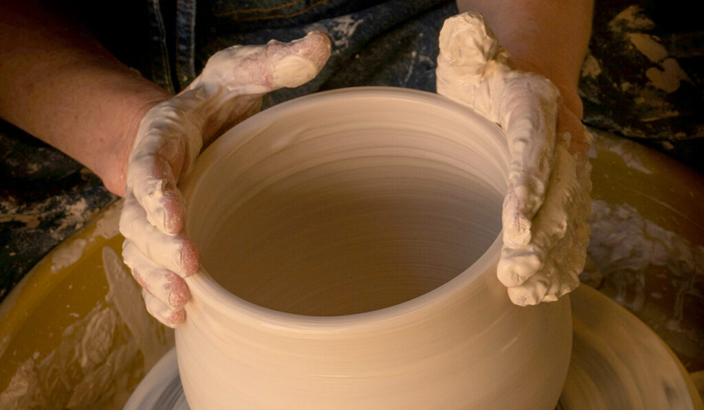 A potter works on wet clay to form a bowl.
