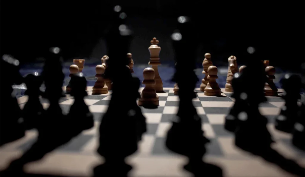 A chessboard with an arrangement of wooden chess pieces, viewed from behind the black pieces with the white king in focus at the center.