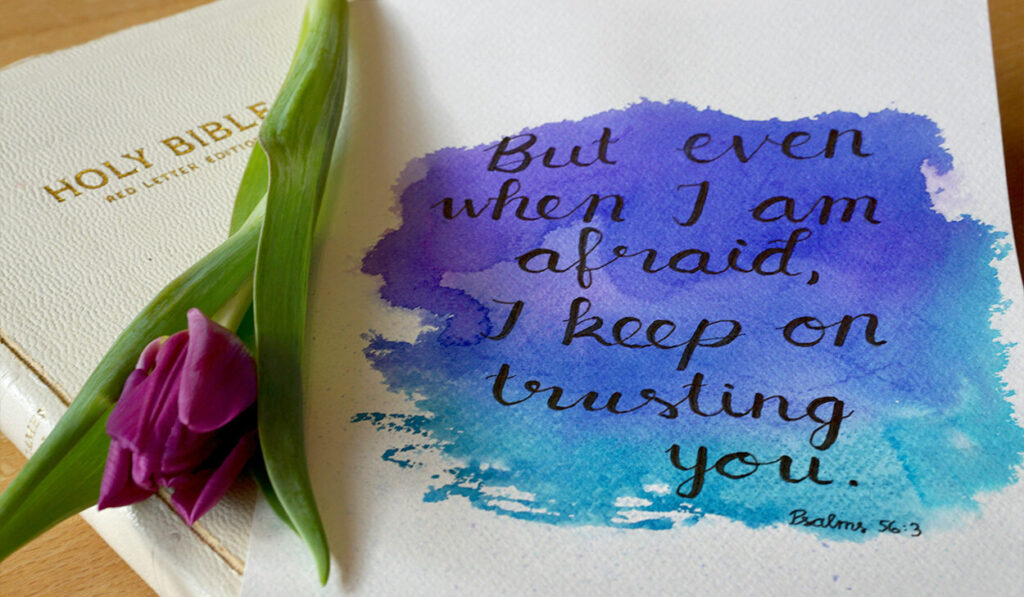 A watercolor print that says, "But even when I am afraid, I keep on trusting you," sits on top of a white Bible next to a purple tulip.