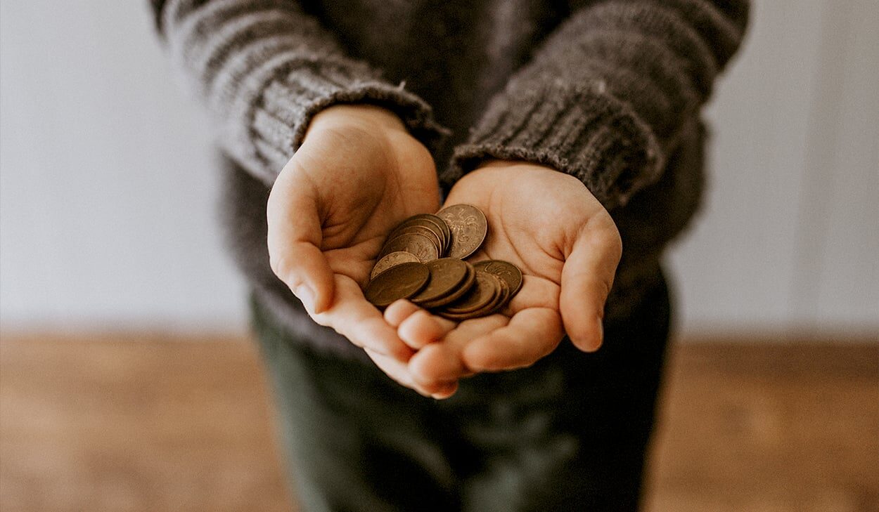 A person wearing a knit sweater holds several small coins in both open hands, with a blurred background.