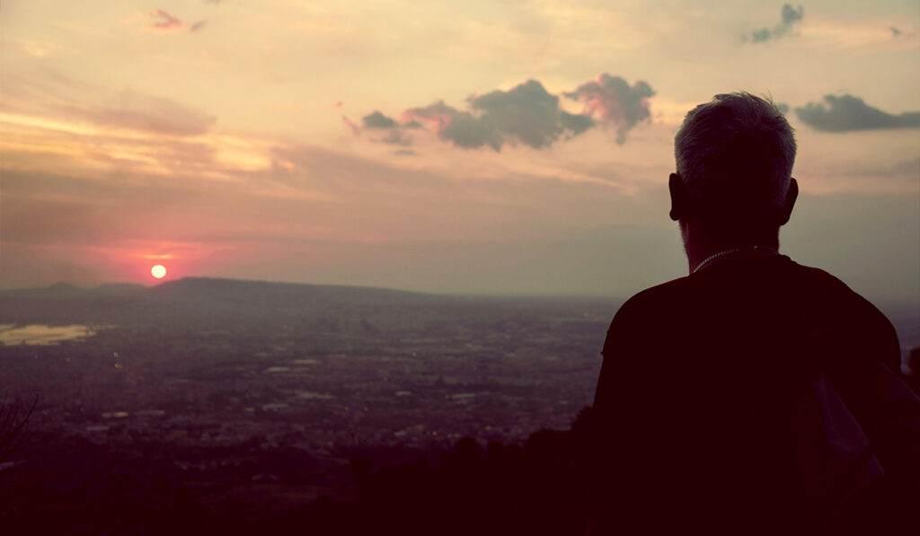 A man in a black shirt looks at a sunset.