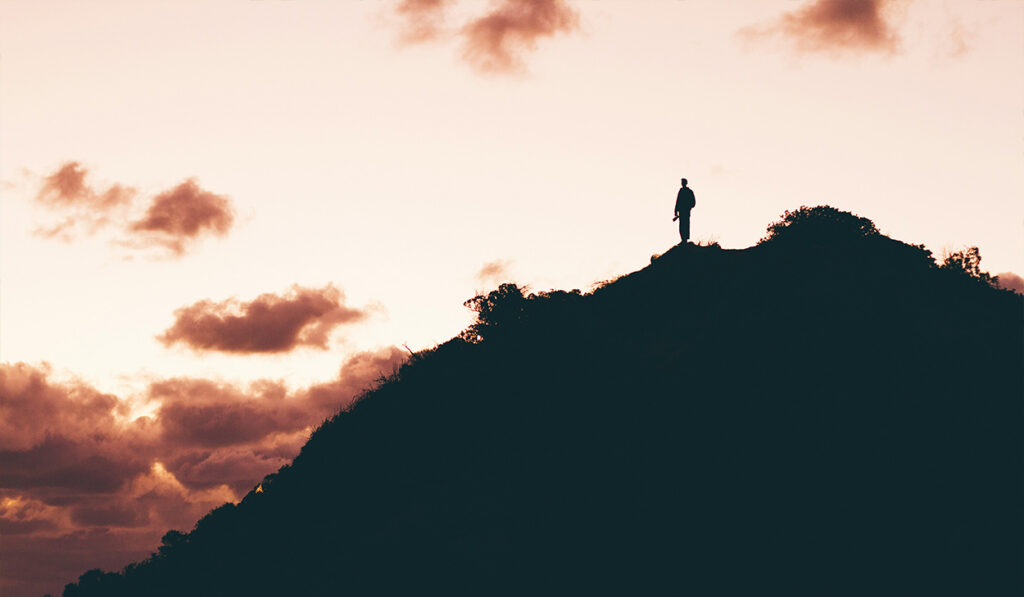 A person stands on a mountain at sunset.