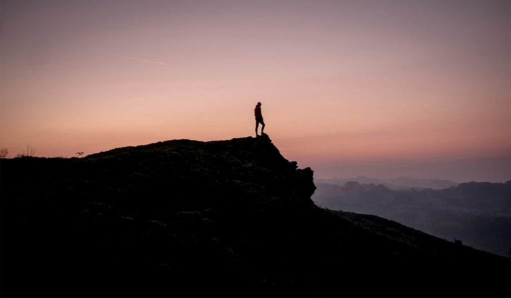 A person stands on a rock formation at sunset.