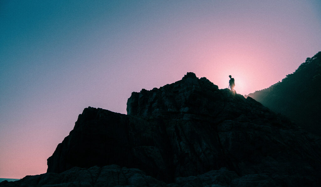 A person stands on a cliff at sunrise.