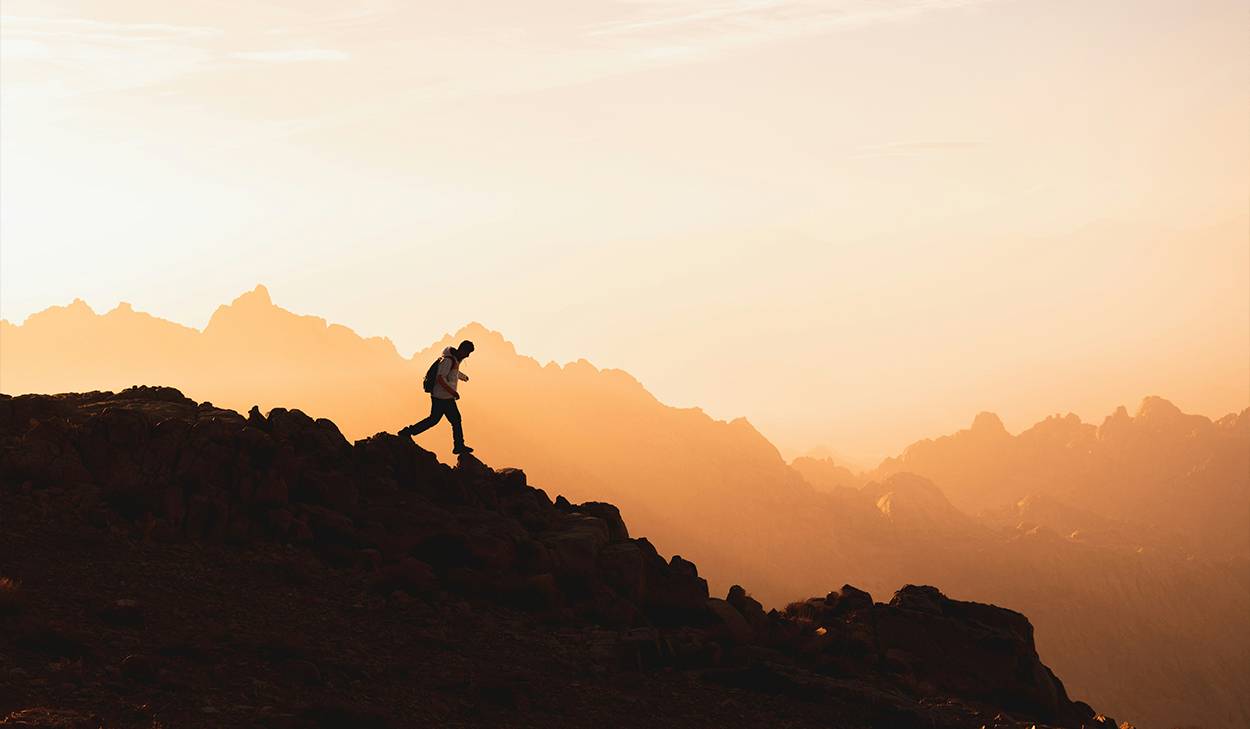 A person in a coat hikes down a rock formation at sunrise.