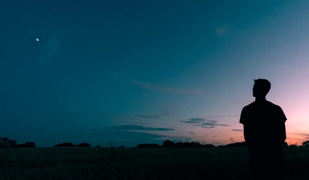 A man looks up at a starry sky.