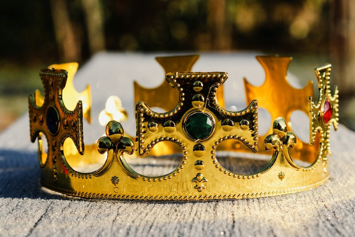 A gold crown decorated with colorful gemstones rests on a wooden surface in natural light.