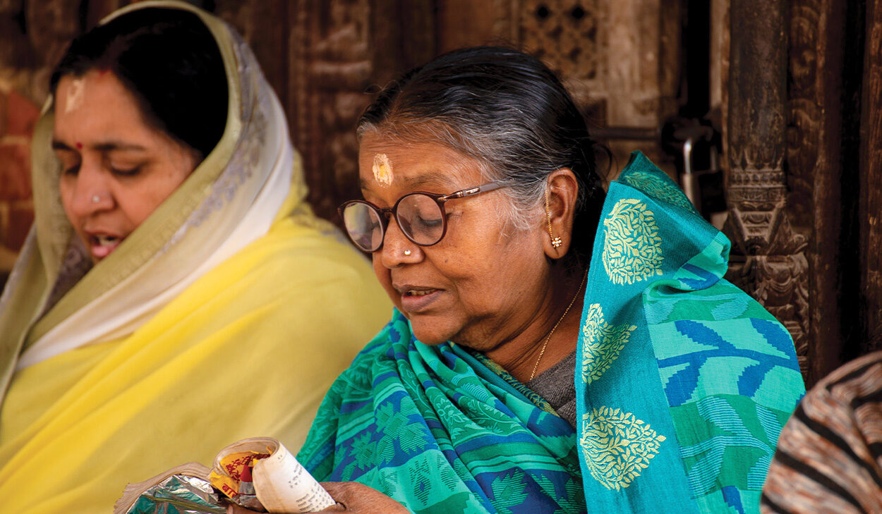 Women in traditional South Asian clothes sit and read together.