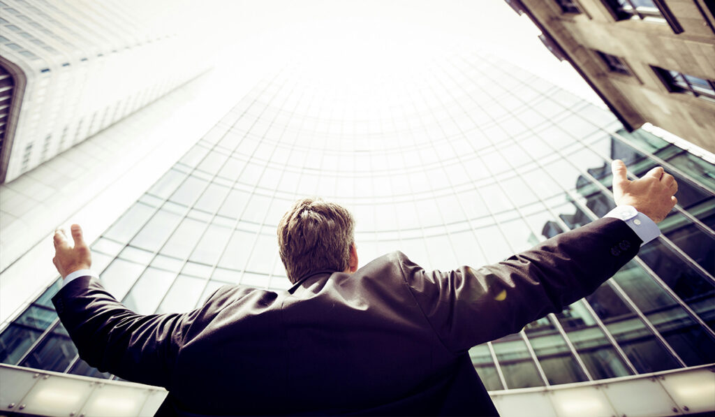 A man in a suit stretches out his arms as he looks up at skyscrapers.