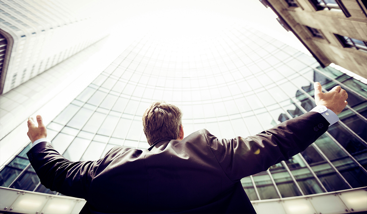 A man in a suit stretches out his arms as he looks up at skyscrapers.