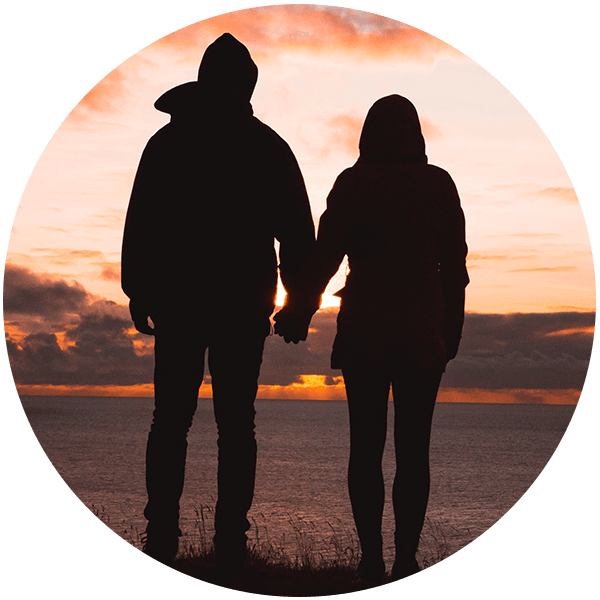 Silhouette of two people holding hands in front of a sunset.